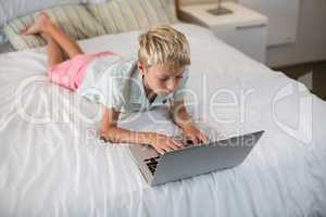 Boy using laptop on bed in bedroom