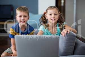 Portrait of siblings with laptop sitting on sofa in living room