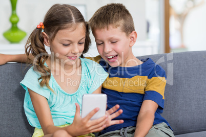 Happy boy sitting on sofa and using mobile phone in living room