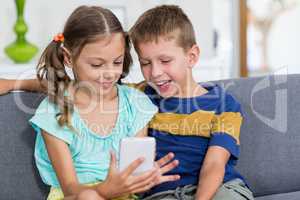 Happy boy sitting on sofa and using mobile phone in living room