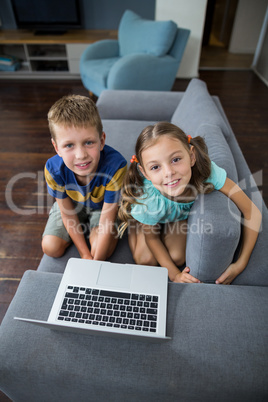 Portrait of siblings with laptop sitting on sofa in living room