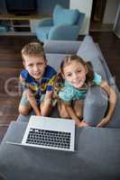 Portrait of siblings with laptop sitting on sofa in living room