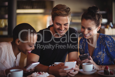 Happy friends using mobile phone while having breakfast Happy friends using mobile phone while having breakfast
