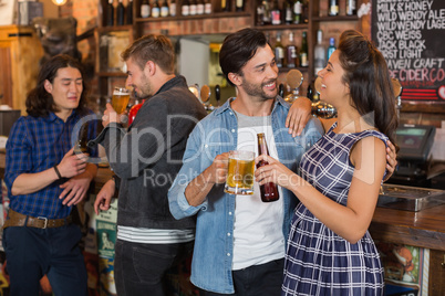 Friends holding beer glass and bottle by counter in pub