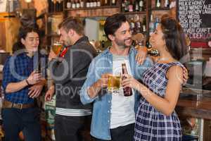 Friends holding beer glass and bottle by counter in pub