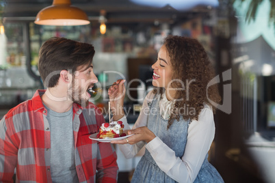 Happy woman feeding cake to male friend