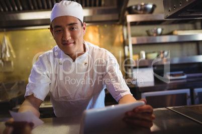 Chef holding digital tablet and an order list in the commercial kitchen