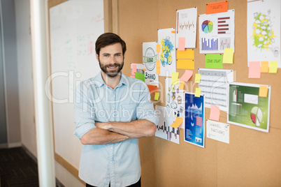 Portrait of young smiling businessman with arms crossed by soft board at office