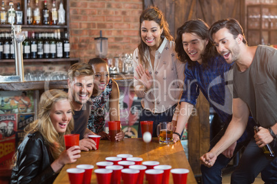 Friends cheering while woman playing beer pong in bar