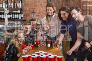 Friends cheering while woman playing beer pong in bar