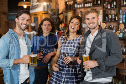 Portrait of friends holding beer glasses and bottles in pub
