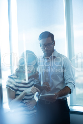Business couple using digital tablet against glass window