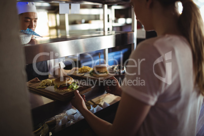 Chef passing tray with french fries and burger to waitress