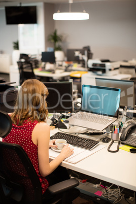 Businesswoman holding coffee cup while working in office