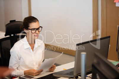 Businesswoman holding documets while looking at laptop