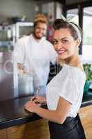 Smiling waitress writing on notepad in kitchen