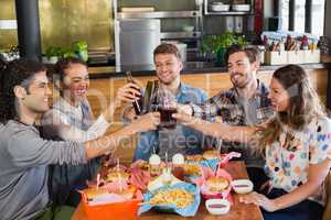 Cheerful friends toasting beer bottles in pub