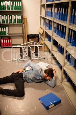 Fallen businessman with file in storage room