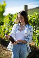 Thoughtful young woman holding wine bottle at vineyard