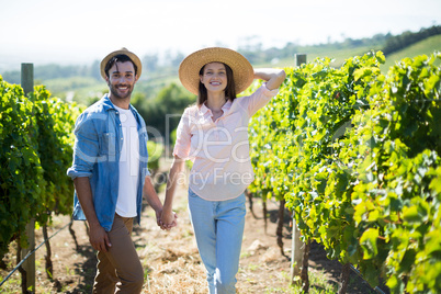 Smiling young couple holding hands at vineyard on sunny day