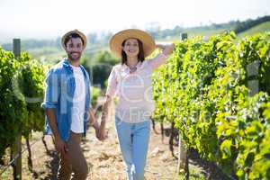 Smiling young couple holding hands at vineyard on sunny day