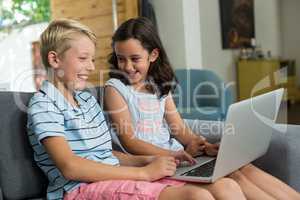 Smiling siblings interacting while using laptop in living room
