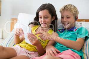 Siblings listening to music while using mobile phone on bed