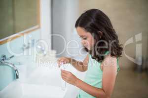 Girl putting toothpaste on brush in bathroom