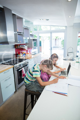 Boy doing his homework while girl using laptop in kitchen