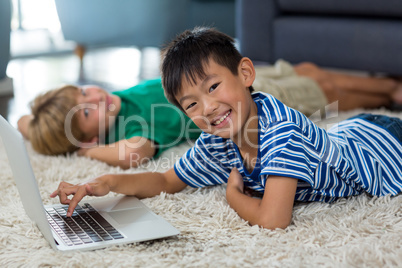 Boy lying on rug and using laptop in living room