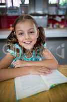 Portrait of smiling girl with book in kitchen