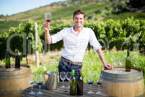 Portrait of young man holding wineglass by table at vineyard