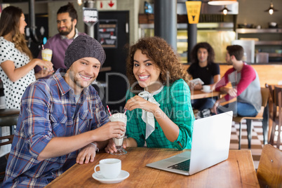 Portrait of smiling couple having milkshake while sitting in restaurant