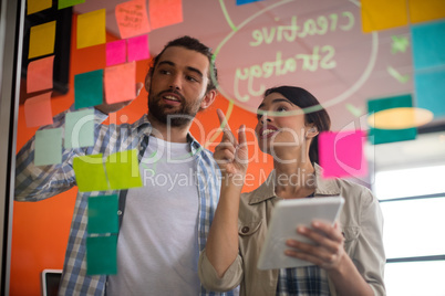 Male and female executives discussing over sticky notes