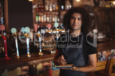Portrait of young waiter writing on diary