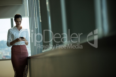Well dressed businesswoman using mobile by window in office