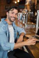 Young man holding beer while sitting by laptop in restarant
