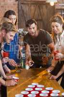 Friends looking at ball while man playing beer pong in bar