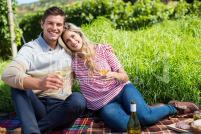 Happy couple holding wineglasses while relaxing on picnic blanket