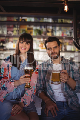 Portrait of happy couple holding glasses of beer at counter