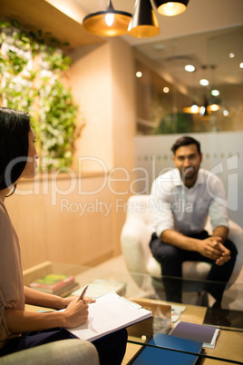 Businesswoman writing on clipboard while discussing with male colleague in office