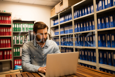 Businessman using laptop in file storage room