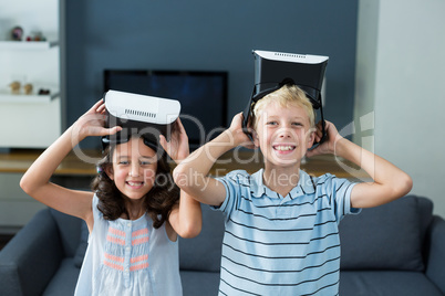 Portrait of siblings holding virtual reality headset in living room