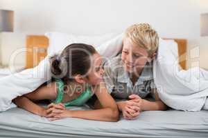 Smiling siblings lying under bed sheet in bedroom