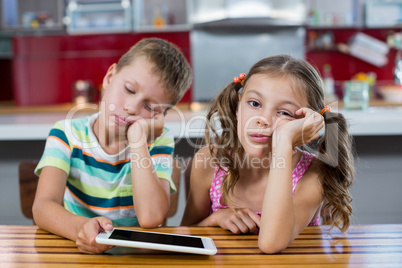 Bored siblings with digital tablet in kitchen