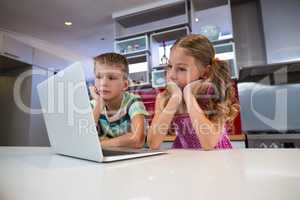 Siblings using laptop in kitchen