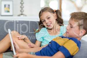 Girl smiling at camera while boy using digital tablet