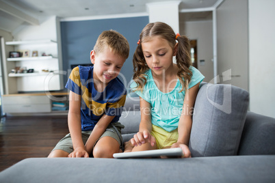 Siblings using digital tablet in living room