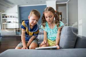 Siblings using digital tablet in living room