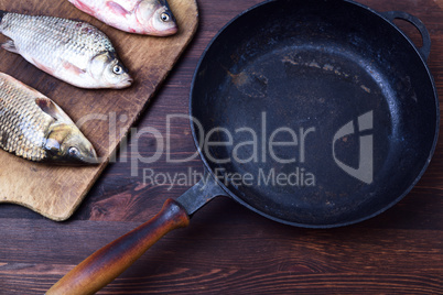 Three fresh carp fish, next to a black cast-iron frying pan